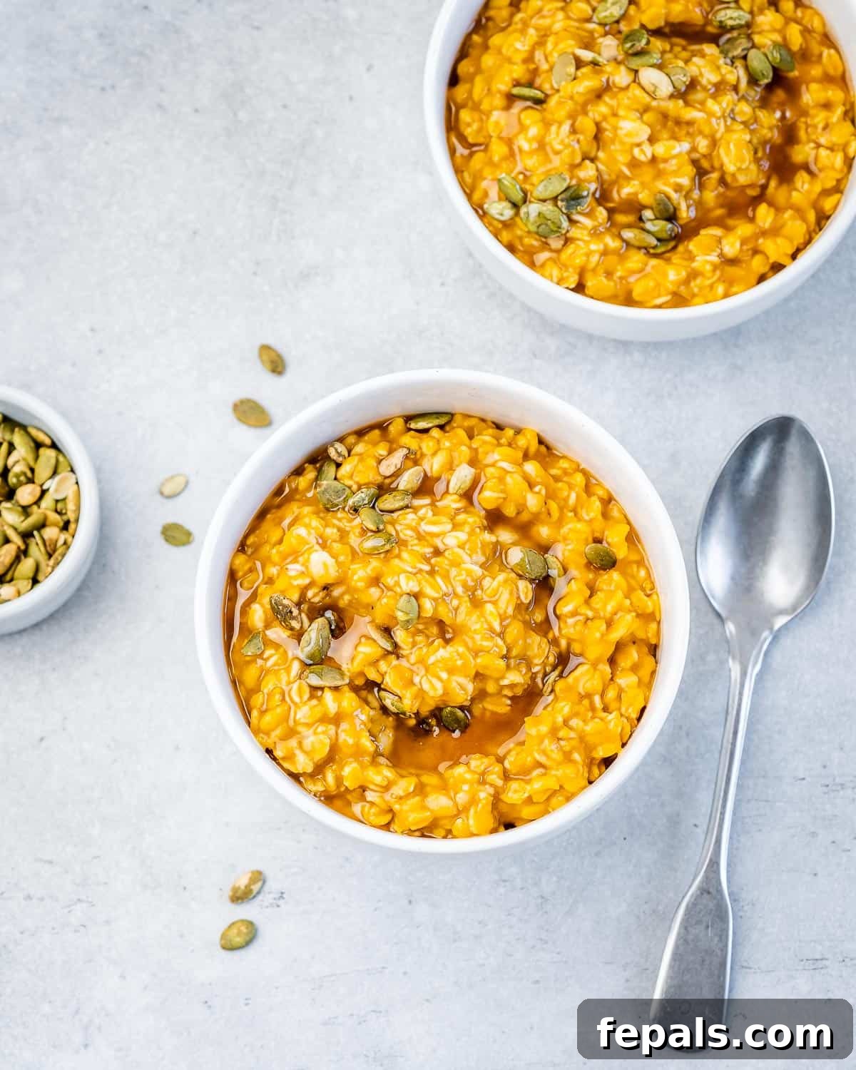 Bowl of oatmeal made with pumpkin and served with maple syrup and pumpkin seeds.