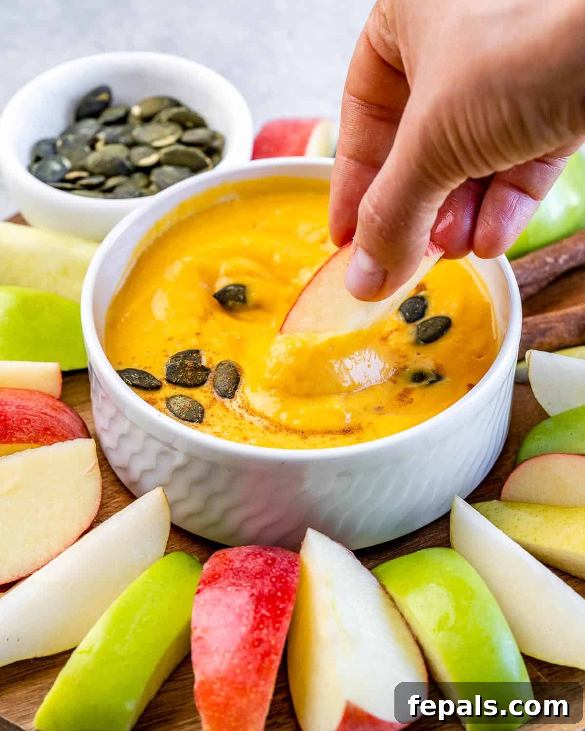 Woman's hand dipping an apple slice into a bowl of pumpkin dip.