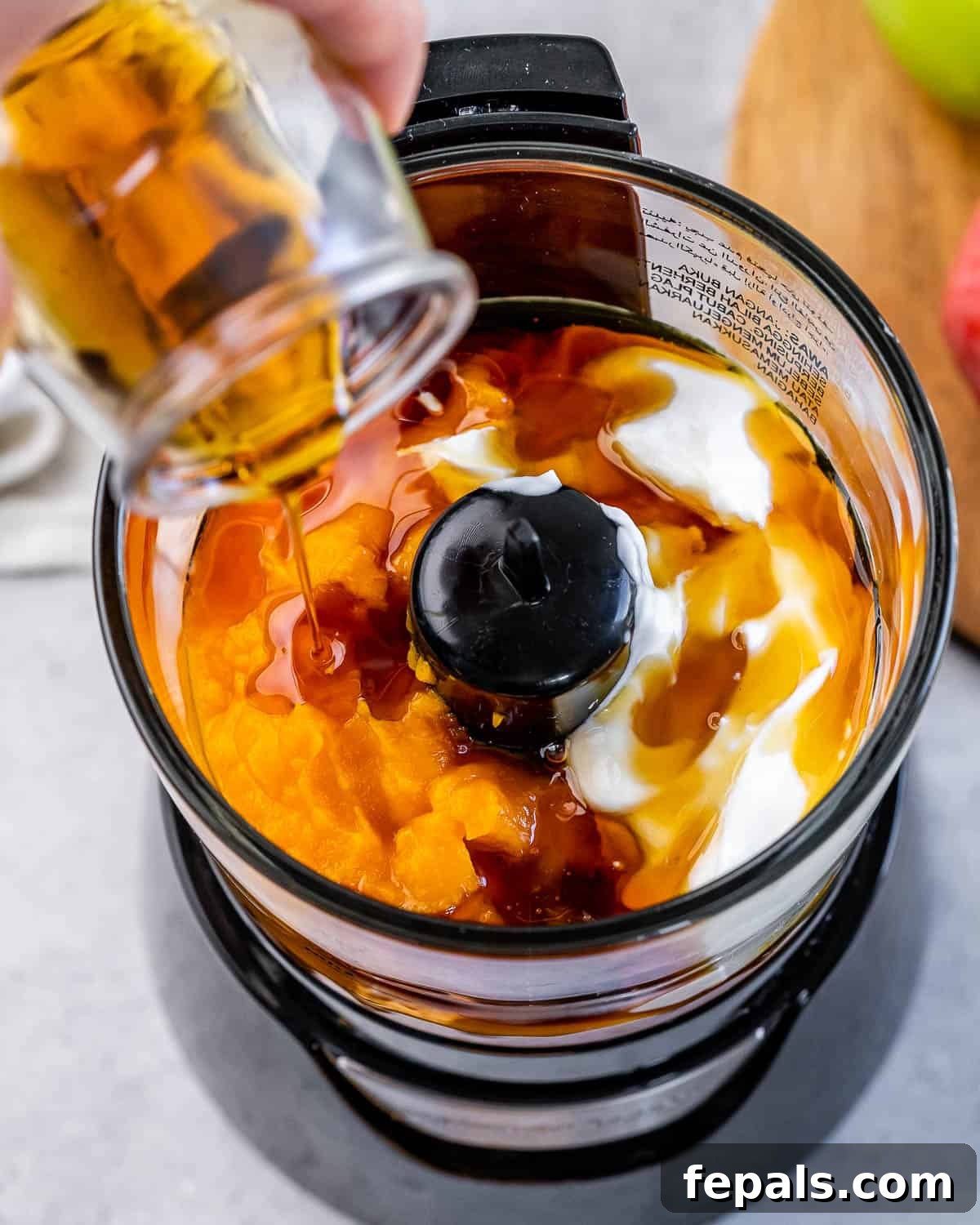 Pouring maple syrup into a food processor with pumpkin and greek yogurt.