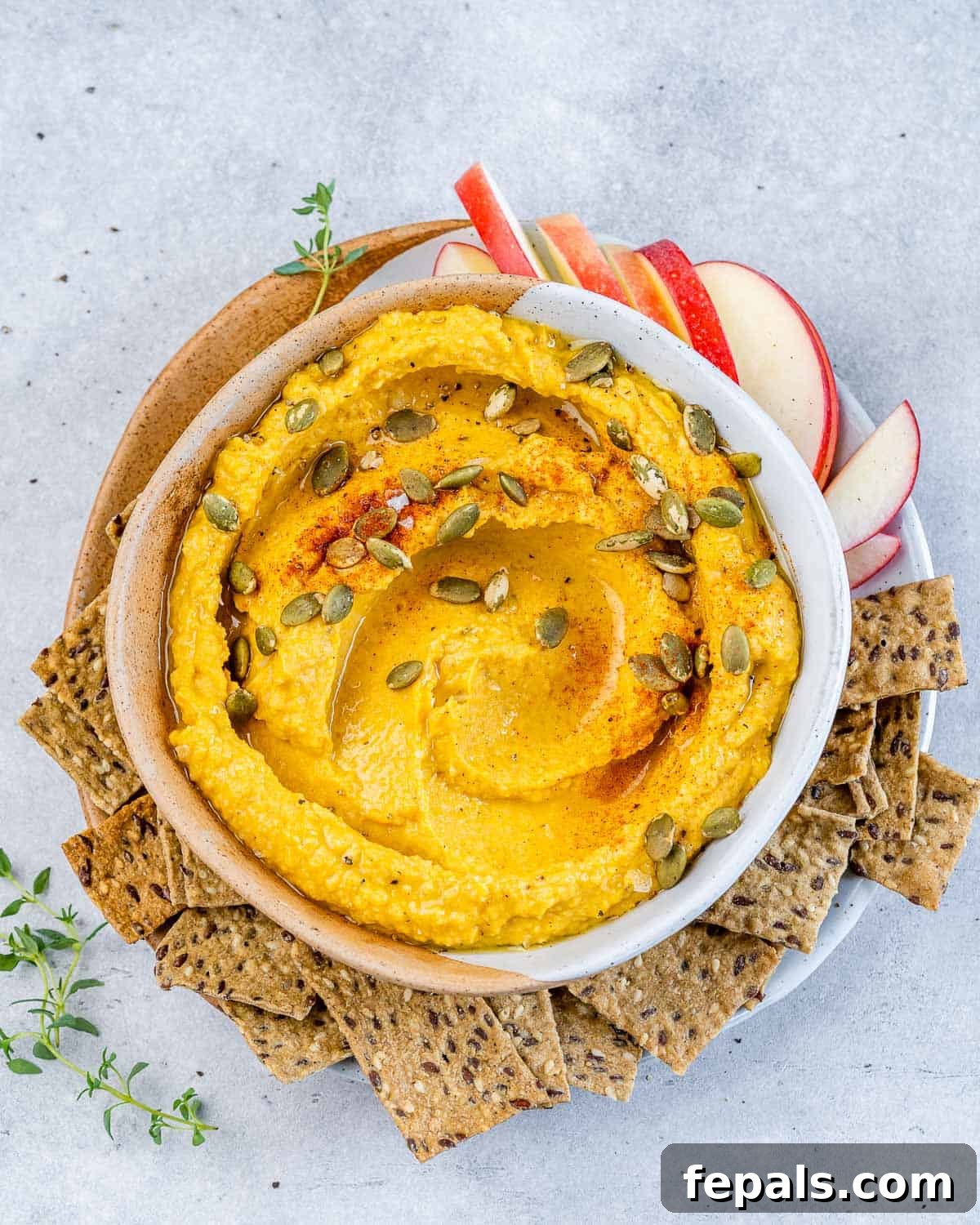 Spiced Pumpkin Hummus 2 Top view of round white bowl with pumpkin hummus that's orange in color, topped with pumpkin seeds and a side of crackers by the bowl.