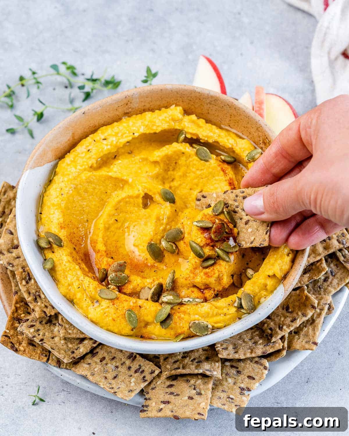 Spiced Pumpkin Hummus 10 Hand dipping a cracker into orange-colored dip.