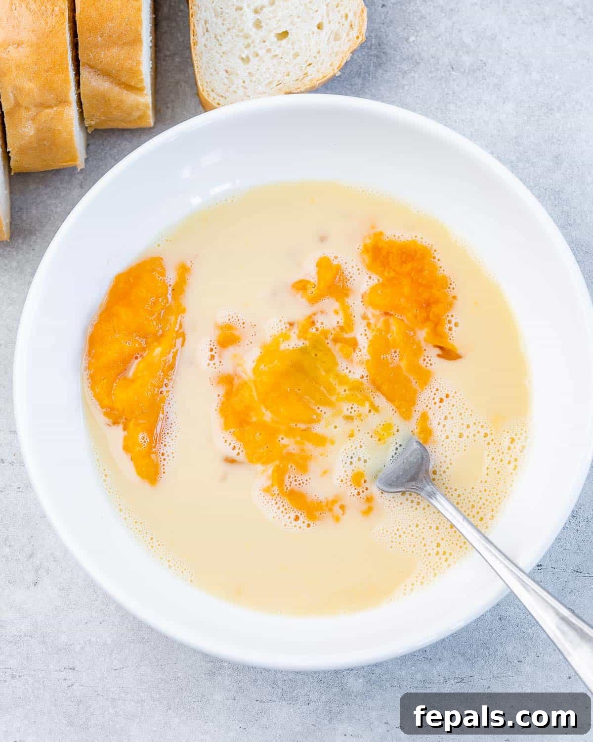 Whisking eggs with pumpkin puree and milk in a bowl.
