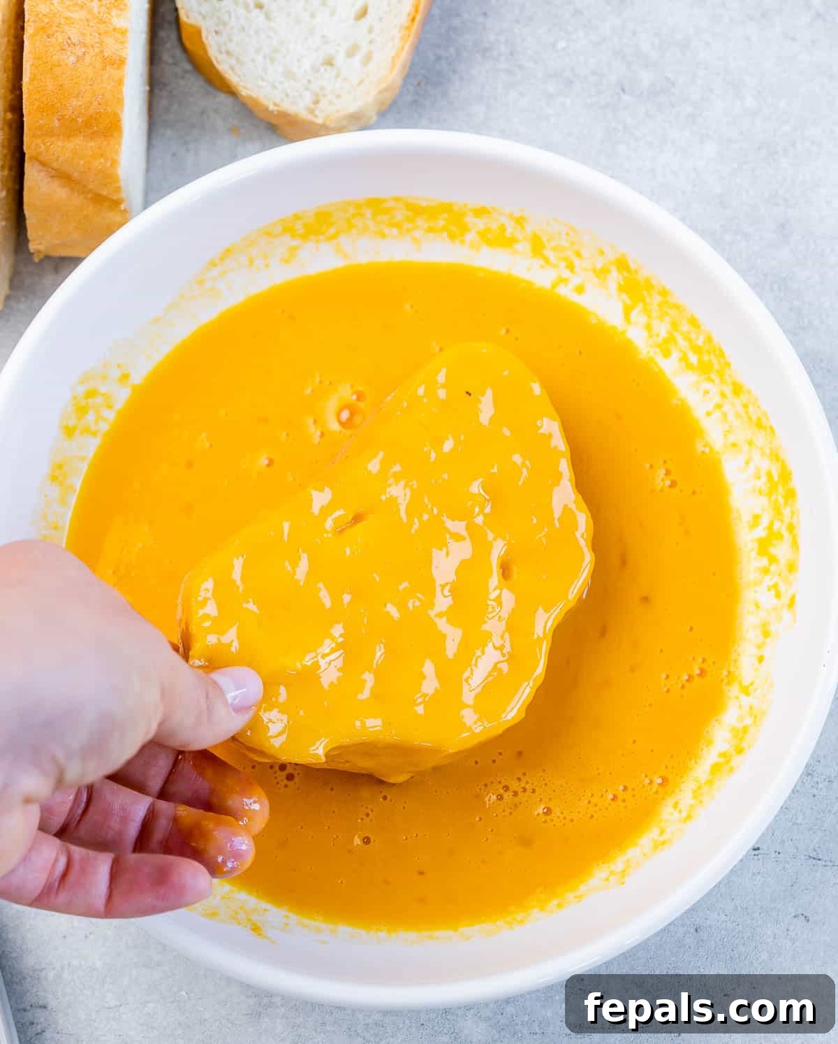 Dipping a slice of bread into an egg and pumpkin custard.