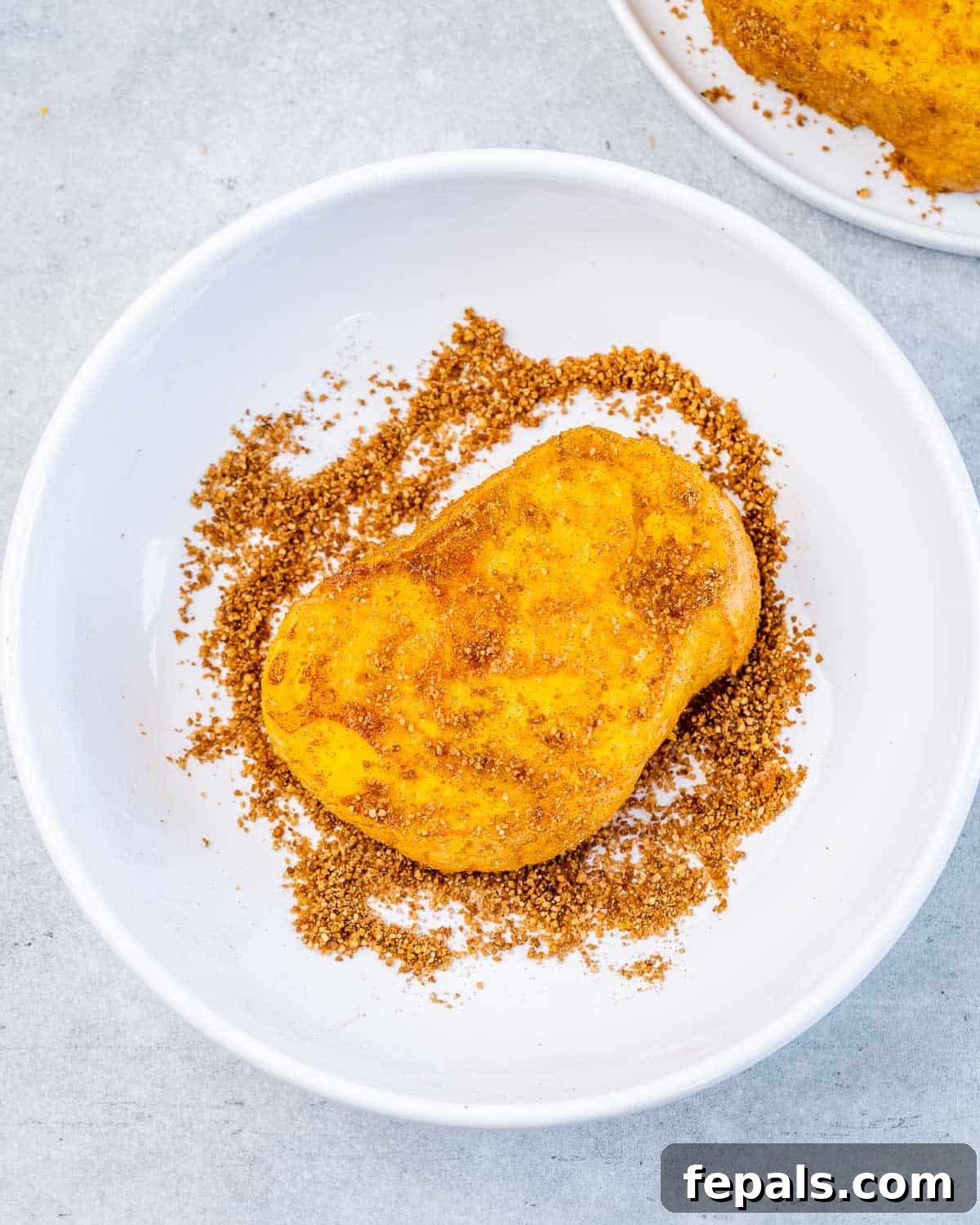 Dredging a slice of French toast in a sugar pumpkin spice mix.