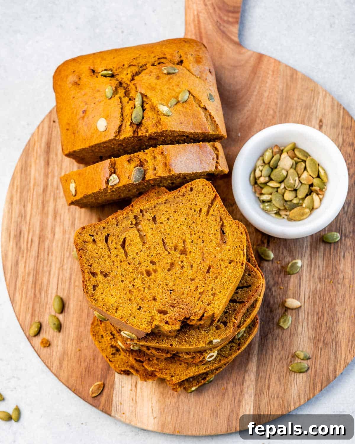 Top view wooden platter with pumpkin bread slices, garnished with pumpkin seeds.