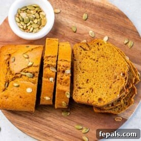wooden platter with pumpkin bread slices. with a small cup of pumpkin seeds on the side of it.