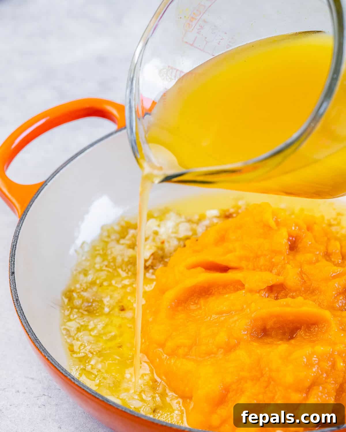 Pouring vegetable broth into a pan with pumpkin mixture, creating a smooth sauce.