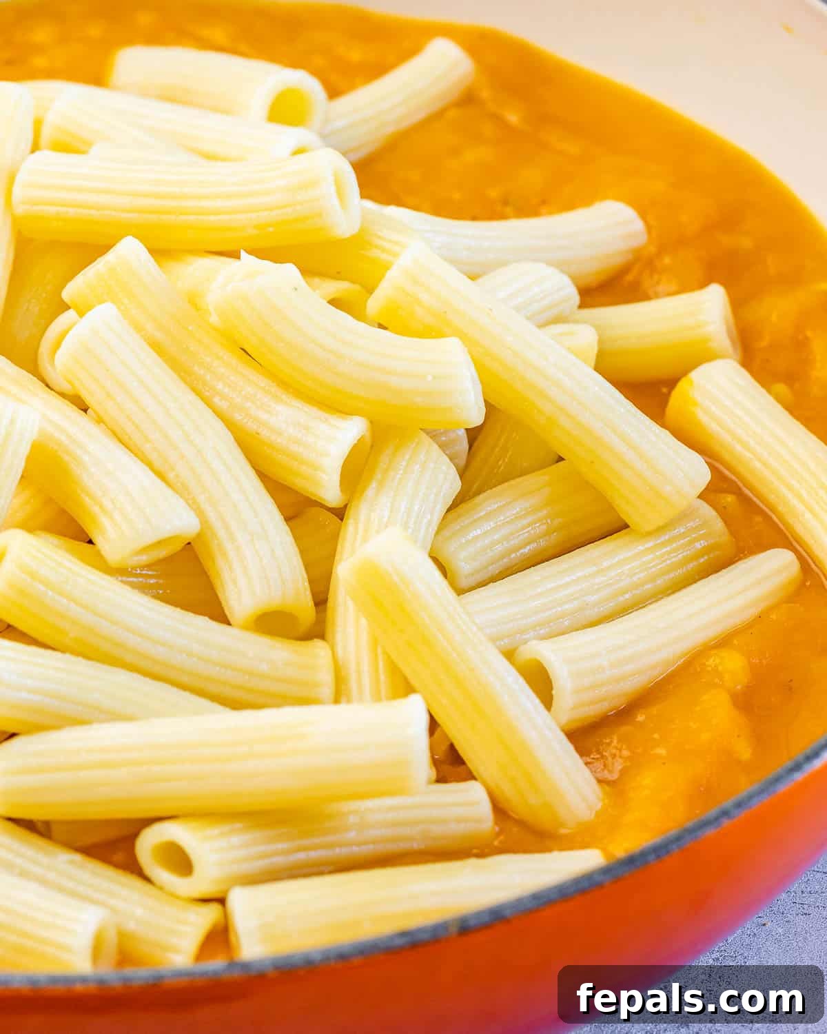 Adding cooked pasta to the creamy pumpkin sauce in a pot, ready to be tossed.