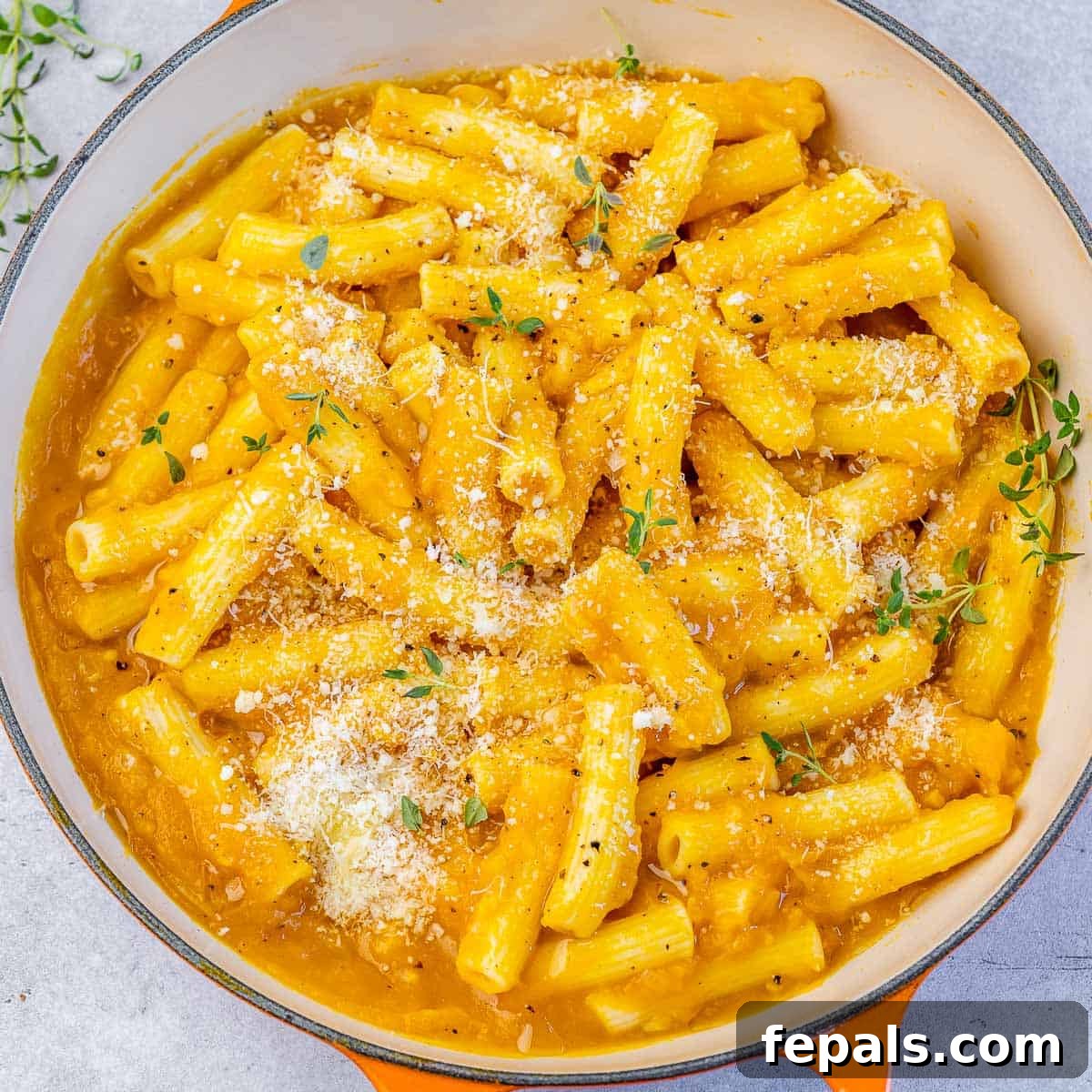 Garnishing a bowl of pumpkin pasta with Parmesan cheese and fresh thyme for presentation.