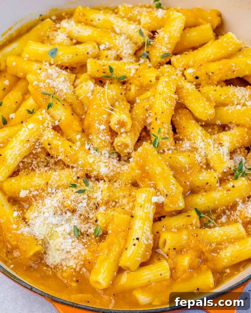 Side shot of creamy pumpkin pasta in a pan, generously garnished with shredded parmesan cheese and fresh herbs, ready to be served.