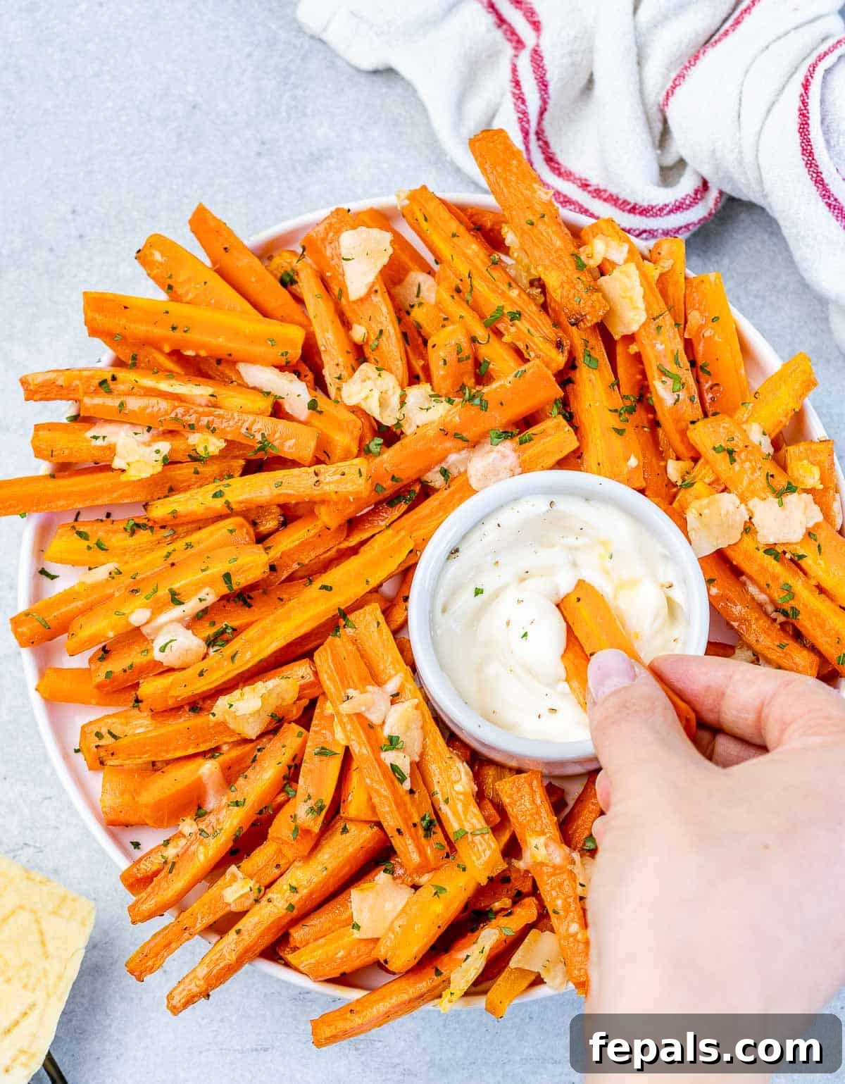 Parmesan Crusted Carrot Fries 11 A hand gently dipping a roasted carrot fry into a small bowl of creamy sauce, emphasizing the perfect bite.