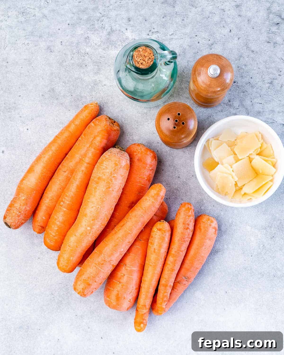 Parmesan Crusted Carrot Fries 4 A simple layout of the core ingredients for roasted carrot fries: large carrots, a wedge of parmesan cheese, a bottle of olive oil, and small bowls of salt and pepper.