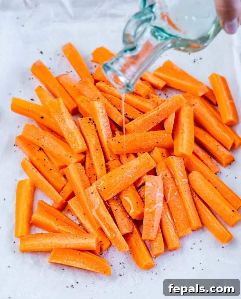Parmesan Crusted Carrot Fries 6 Olive oil being drizzled over the cut carrot strips on a baking sheet, preparing them for seasoning.