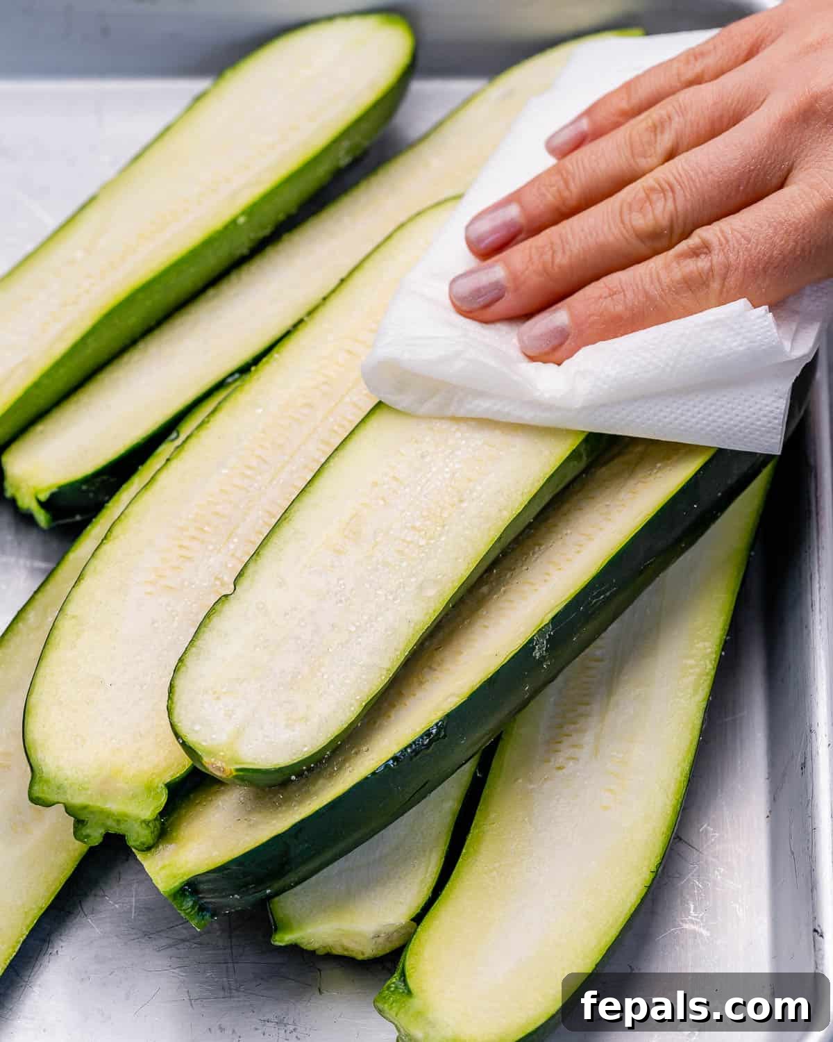 Patting zucchini dry with a paper towel.