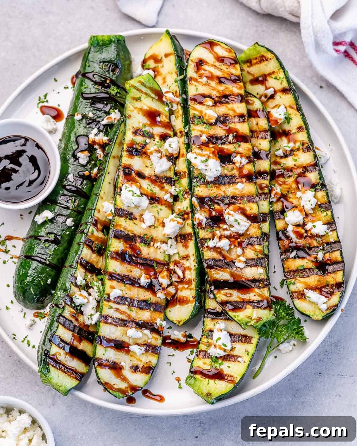 Grilled zucchini on a white plate served with balsamic glaze.