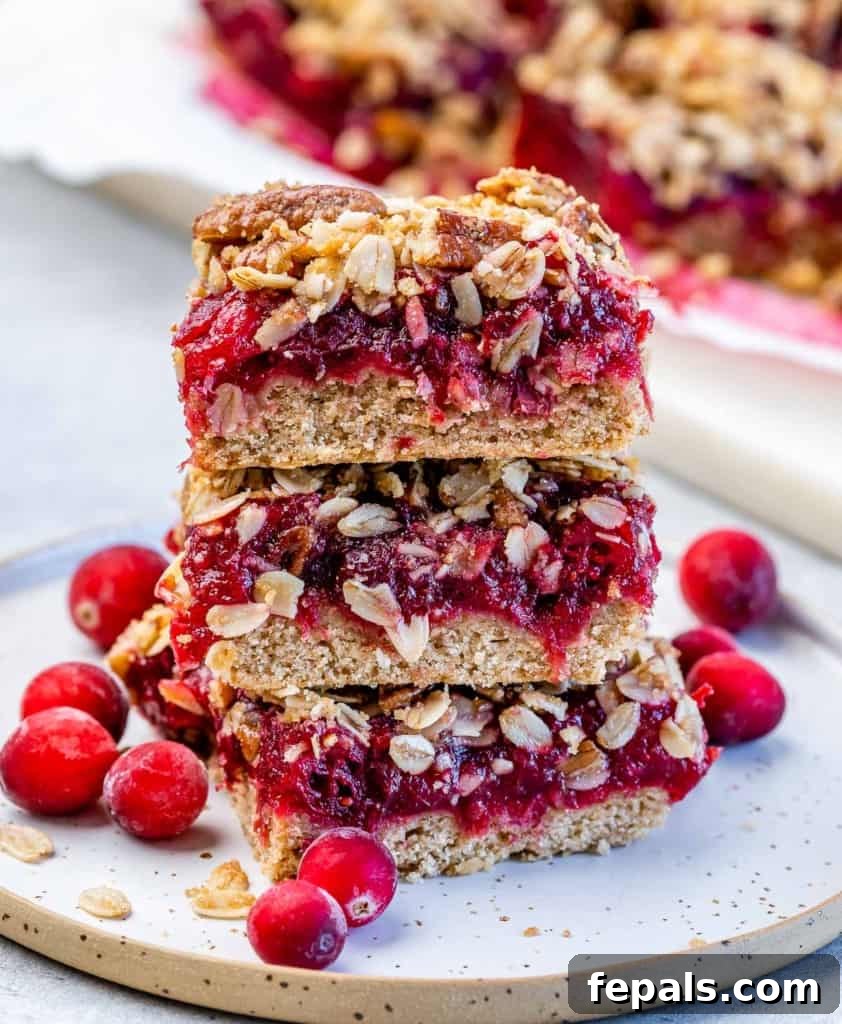 Side shot of 3 cranberry stuffed oat bars stacked on each other on a white plate, garnished with fresh cranberries.