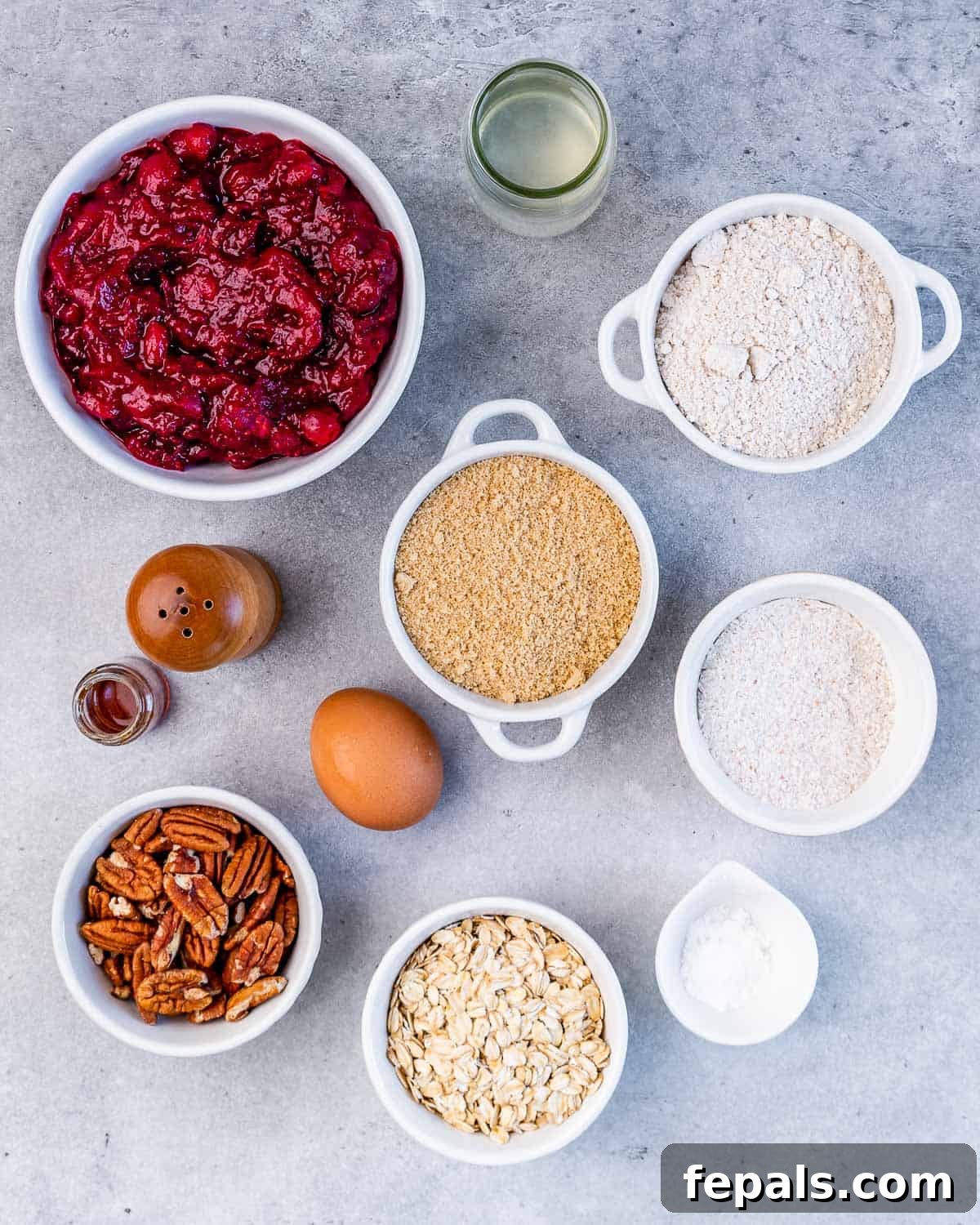 Cranberry sauce, flour, oats, sugar, egg and pecans laid out on a surface, ready for baking.