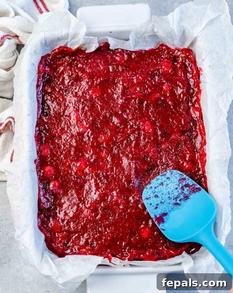 Spreading cranberry sauce over a baked cookie crust in a baking dish.