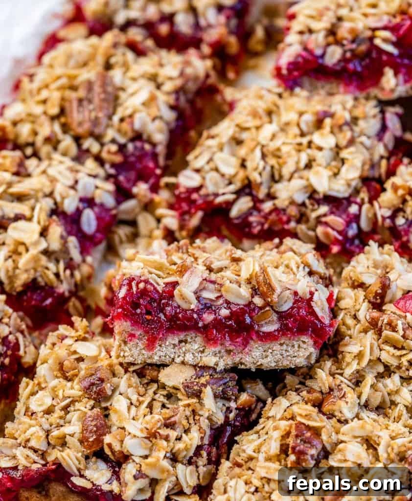 Close up of baked cranberry bars cut into squares on a parchment paper, showing the texture and layers.