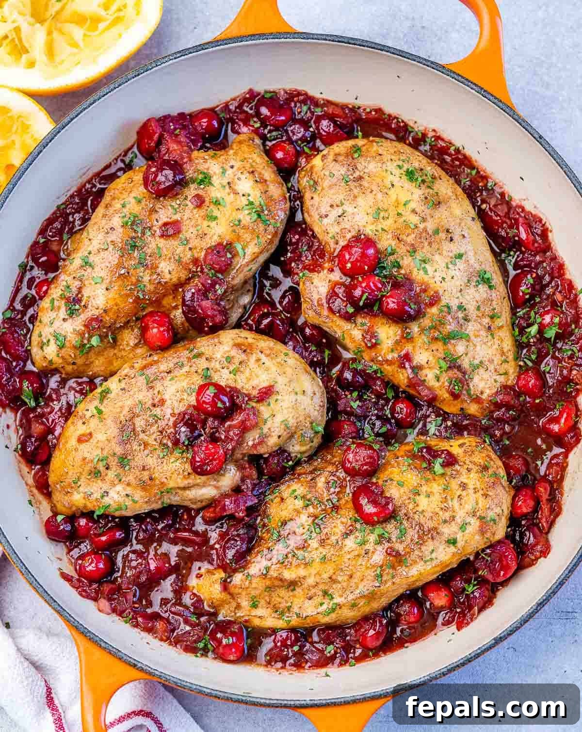 Top view of a skillet with 4 cooked chicken breast in a cranberry sauce, garnished with fresh herbs.