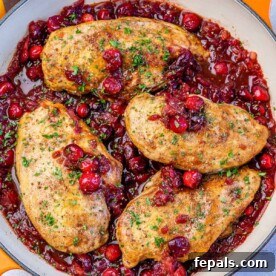 Top view of a skillet with 4 cooked chicken breast in a cranberry sauce.