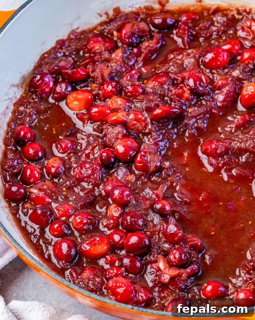 Making cranberry sauce in a large pan with red onion, cranberries, and orange zest.