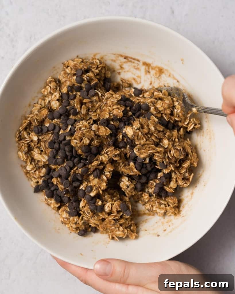 Spiced Pumpkin Power Morsels 11 A fork gently stirring mini chocolate chips into the pumpkin oat mixture, ensuring even distribution.
