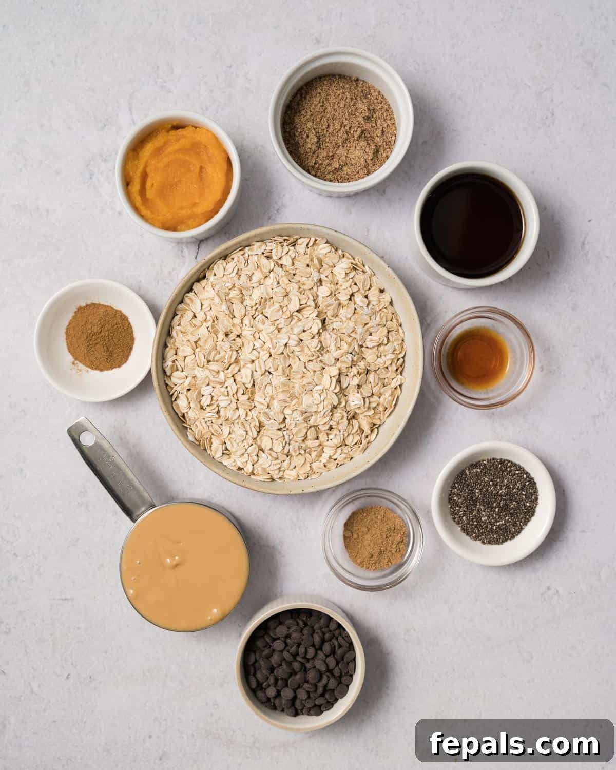 Spiced Pumpkin Power Morsels 4 Various ingredients for pumpkin pie energy bites laid out in small bowls: oats, peanut butter, maple syrup, chia seeds, flaxseed, pumpkin puree, and warm spices.