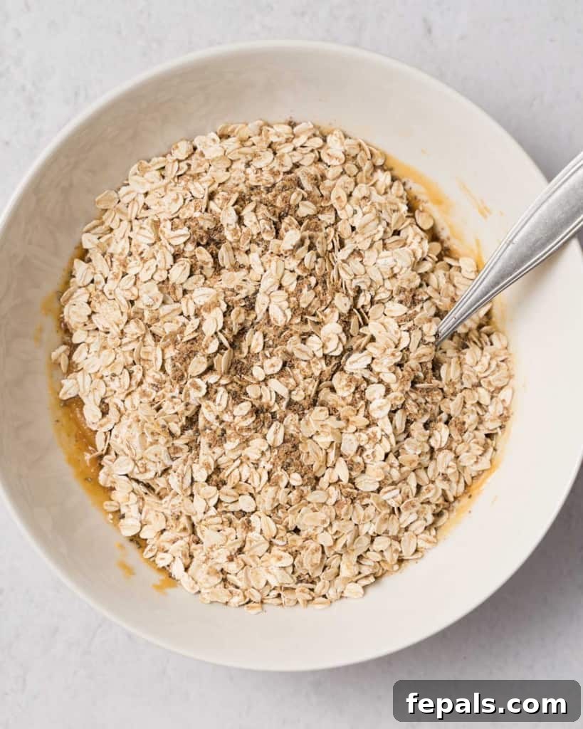 Spiced Pumpkin Power Morsels 8 The oat mixture being thoroughly stirred with the peanut butter and pumpkin blend in a large bowl, ensuring an even consistency.