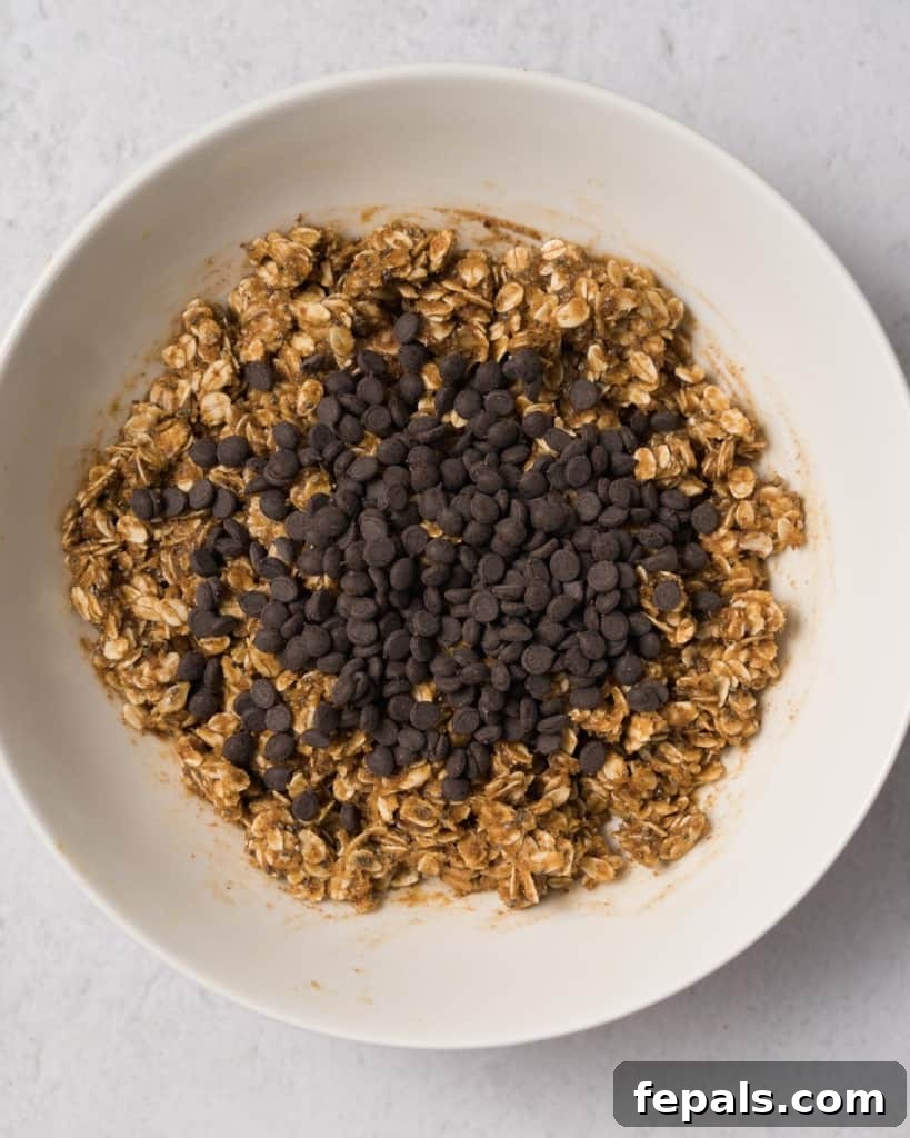 Spiced Pumpkin Power Morsels 10 Mini chocolate chips being added to the mixed oat and pumpkin dough in a bowl.