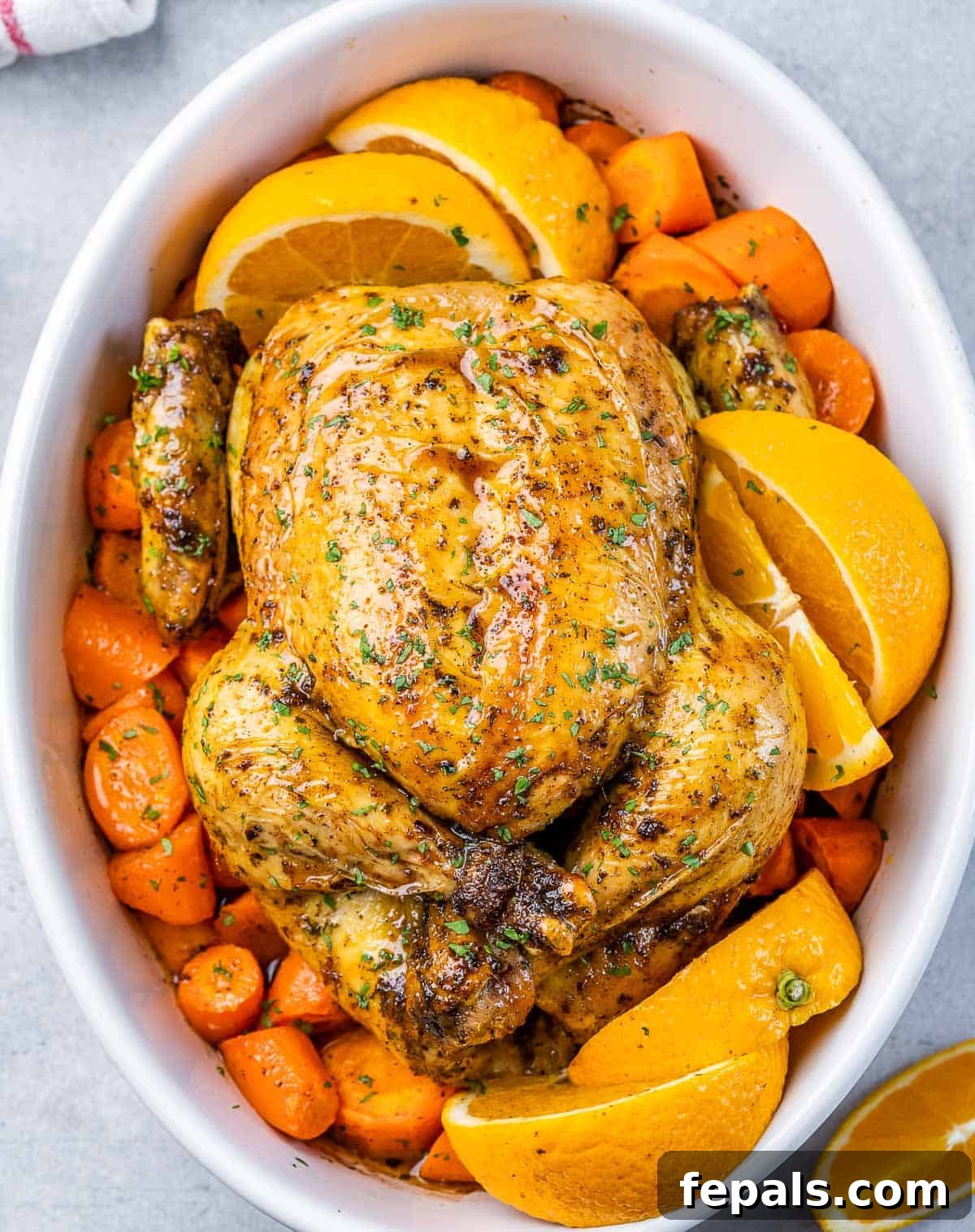 Maple-Kissed Roasted Whole Chicken 2 Top view of a whole baked chicken over chopped carrots in a white dish, garnished with fresh parsley.