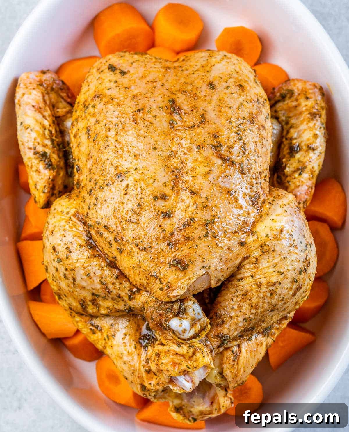 Maple-Kissed Roasted Whole Chicken 6 Seasoned whole chicken placed in a baking dish over chopped carrots.