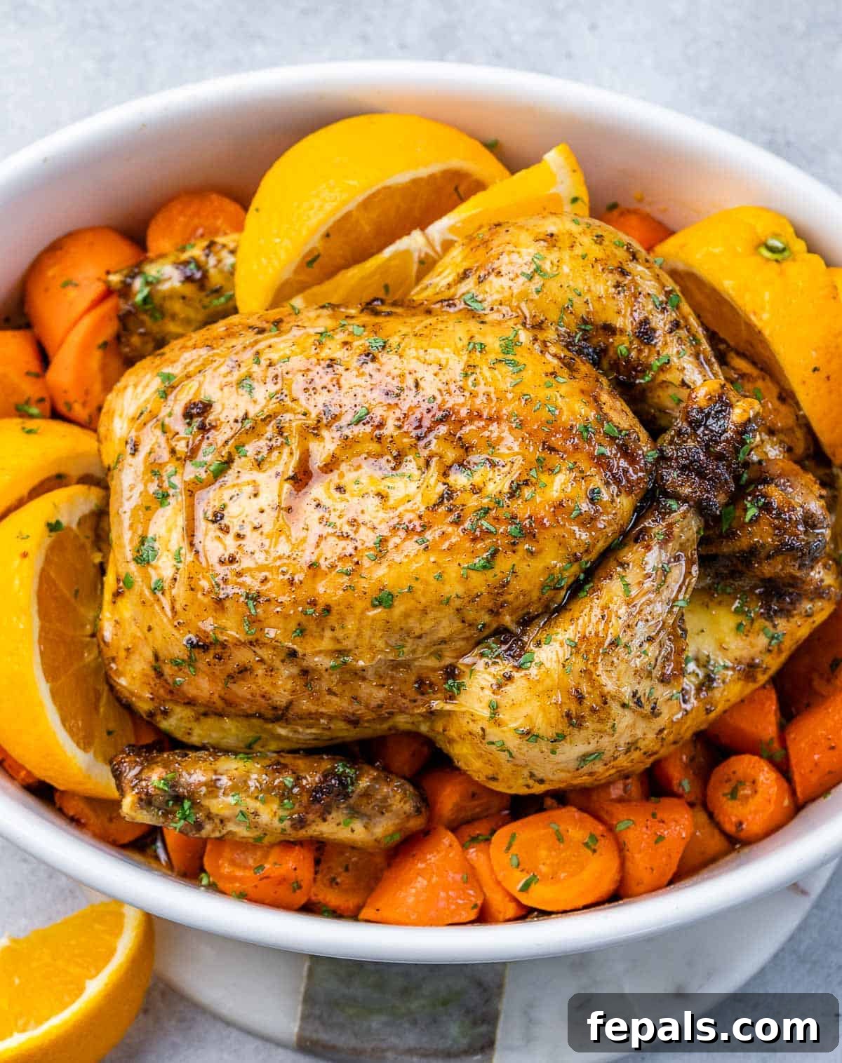 Maple-Kissed Roasted Whole Chicken 9 A white baking dish with a whole baked chicken over chopped carrots and vibrant orange slices, ready to be served.
