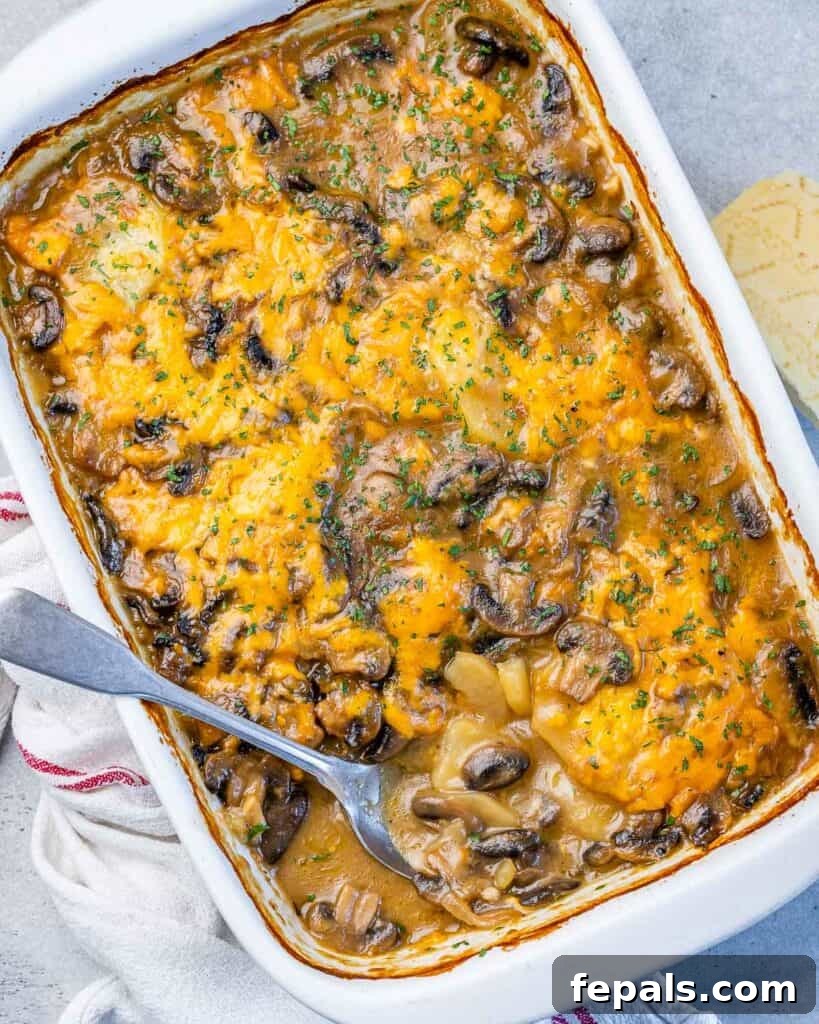 Top view of a white baking dish filled with a baked scalloped potato and mushroom casserole, featuring a creamy and golden-brown cheese topping.