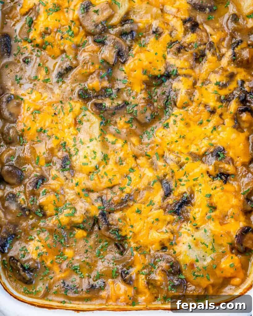 Close-up, top view of a freshly baked potato and mushroom casserole, generously topped with melted, golden-brown cheese.