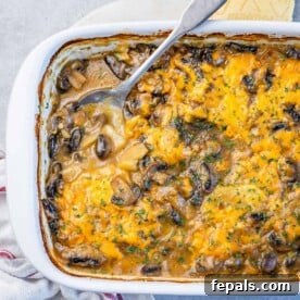 Top view of a white dish with creamy potato and mushroom casserole with spoon in the dish