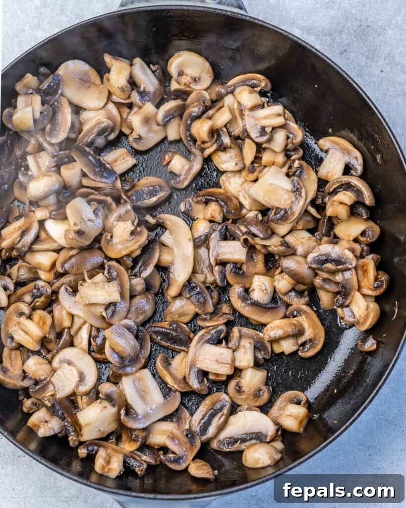Close-up shot of sautéed mushrooms sizzling in a black skillet on the stovetop, releasing their moisture and browning.