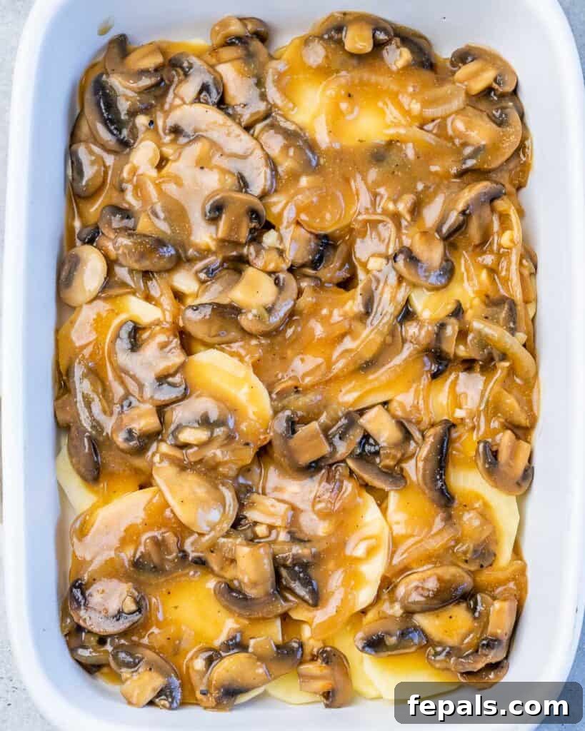 A white baking dish with thinly sliced potatoes, topped with a rich mushroom sauce, demonstrating the layering process.