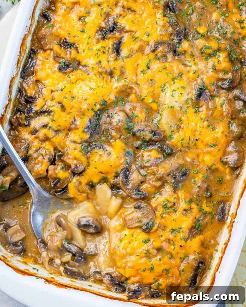 Close-up, top view of a baked cheesy potato and mushroom casserole, with a serving spoon positioned on the lower-left side of the dish.