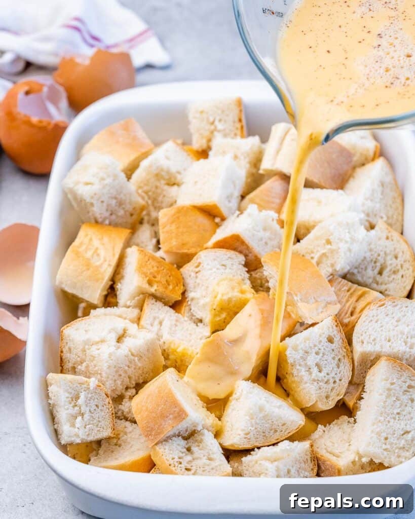 Pouring egg custard mixture over cubed bread in a casserole dish.