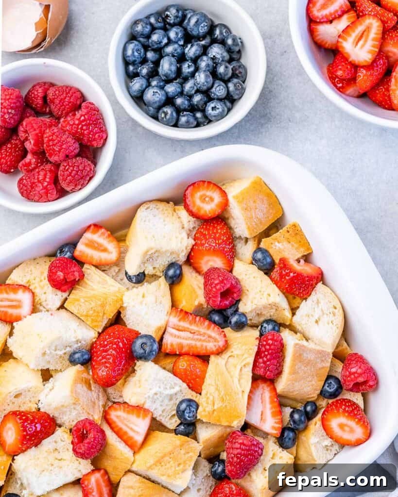 Adding fresh mixed berries over the bread and custard in a casserole dish.