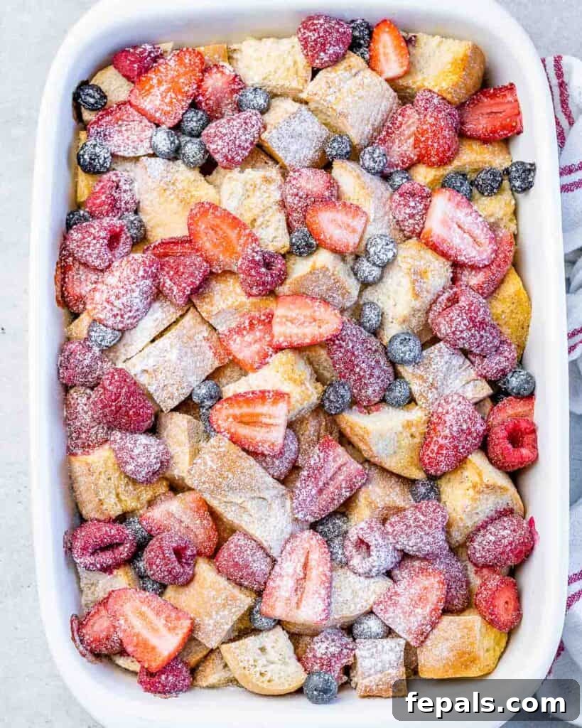 top view of a white dish with baked french toast topped with fresh cut berries and white powder sugar