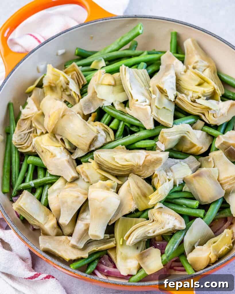 Mediterranean Artichoke Green Bean Bake 7 green beans and artichoke added over sauteed onions in an orange skillet