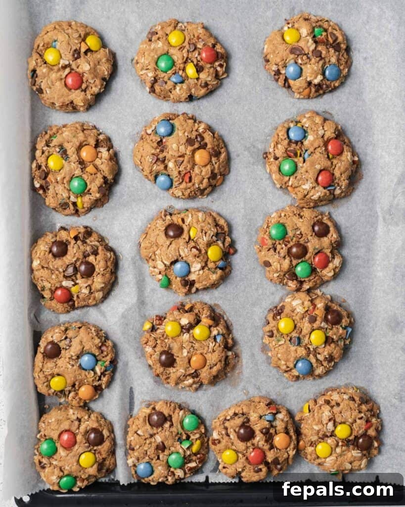 Baked cookies with colorful M&M's and melted chocolate chips on a parchment-lined baking sheet.
