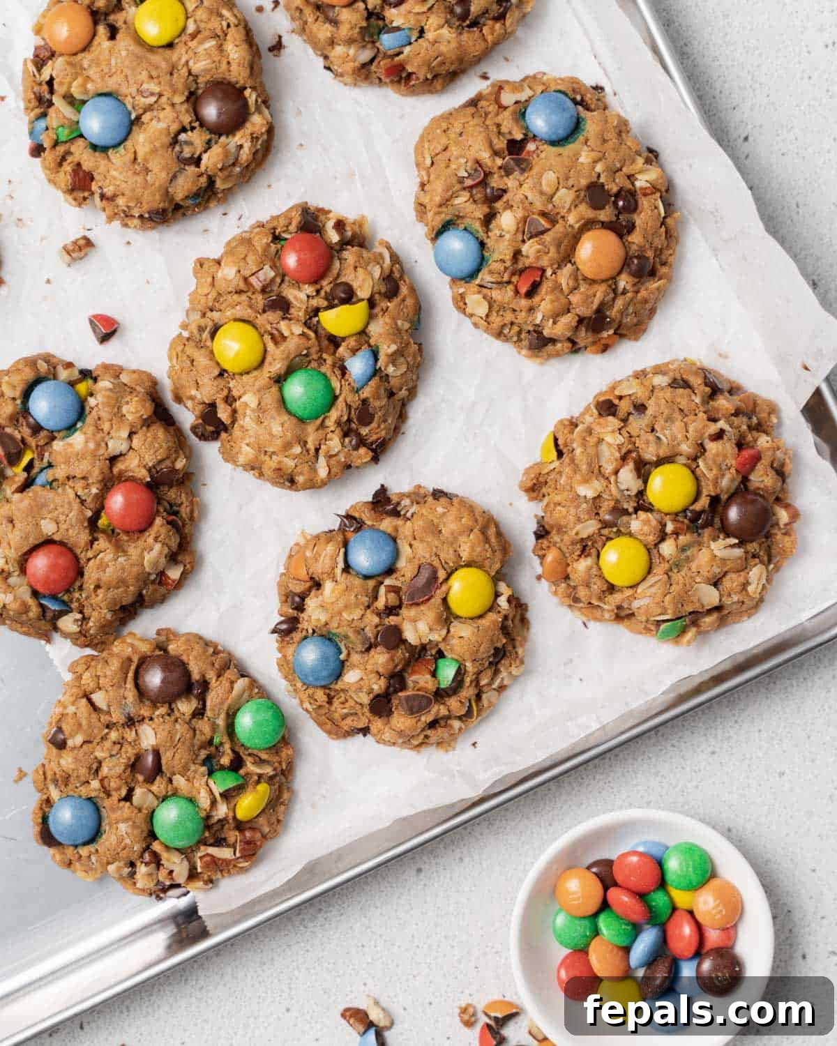 Close-up of freshly baked gluten-free monster cookies cooling on parchment paper, showing the vibrant M&M's and chocolate chips.