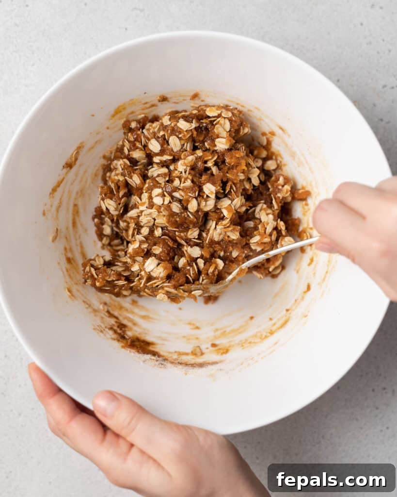 Stirring wet ingredients with oats in a white bowl, showing the beginning stages of cookie dough.