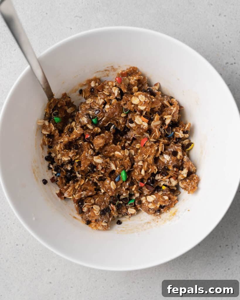Stirring together the colorful cookie dough batter in a large white bowl to evenly distribute all mix-ins.