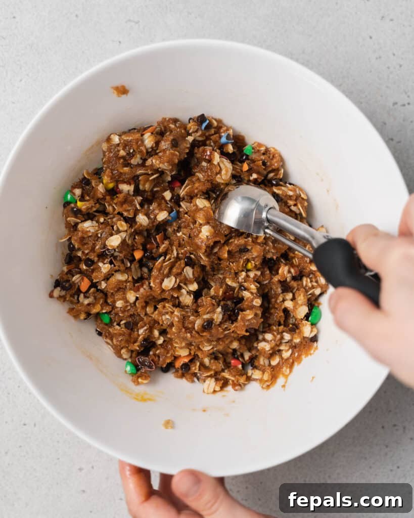 Scooping cookie dough out of a white bowl with a metal cookie scoop.