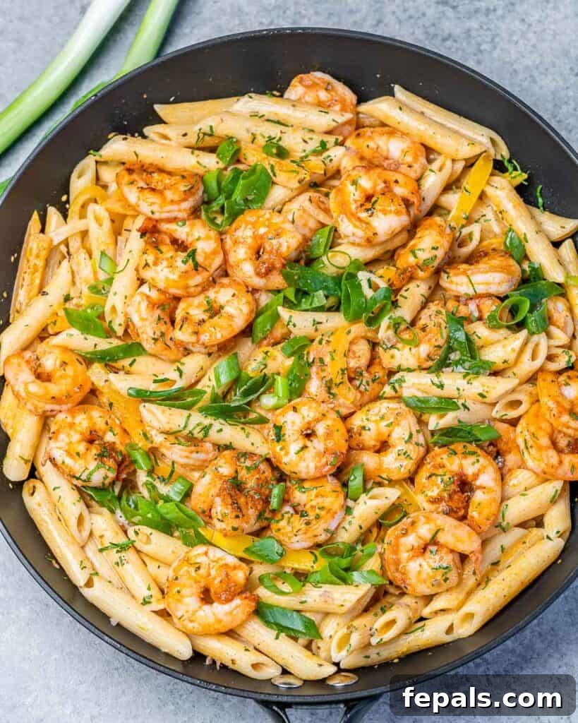 Top view of a black skillet filled with creamy Jamaican Shrimp Rasta Pasta, garnished with fresh green onions.