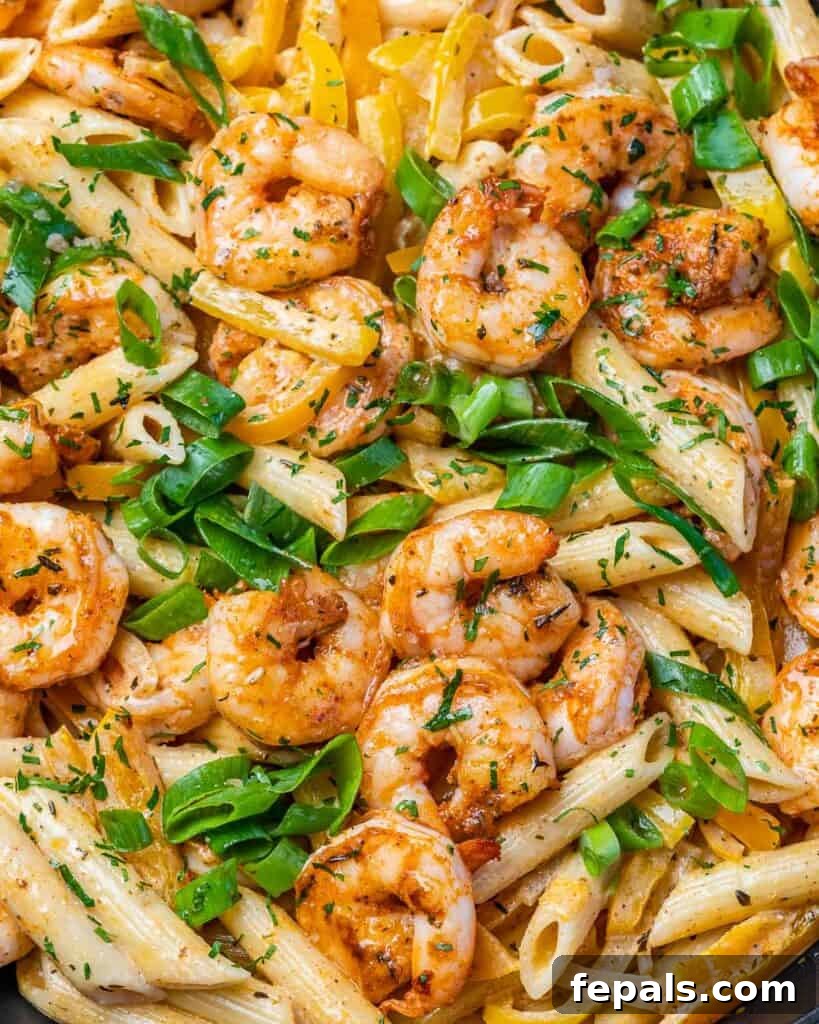 Close-up view of cooked shrimp in a creamy orange sauce with penne pasta, garnished with sliced green onions, showcasing the vibrant colors of Rasta Pasta.